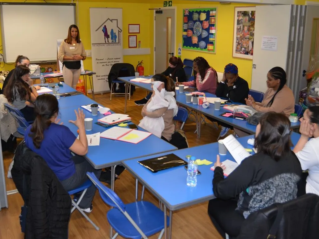 Mothers taking part in a Mothers' Springboard workshop, seated around tables while a facilitator speaks