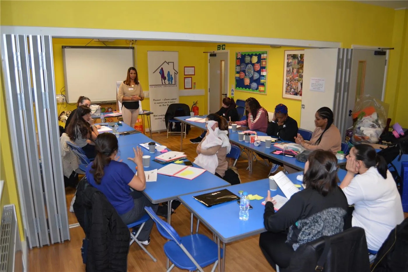 Mothers taking part in a Mothers' Springboard workshop, seated around tables while a facilitator speaks